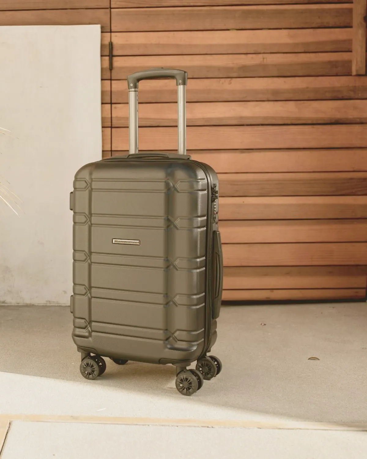 Dark hard-shell cabin suitcase standing against a timber wall
