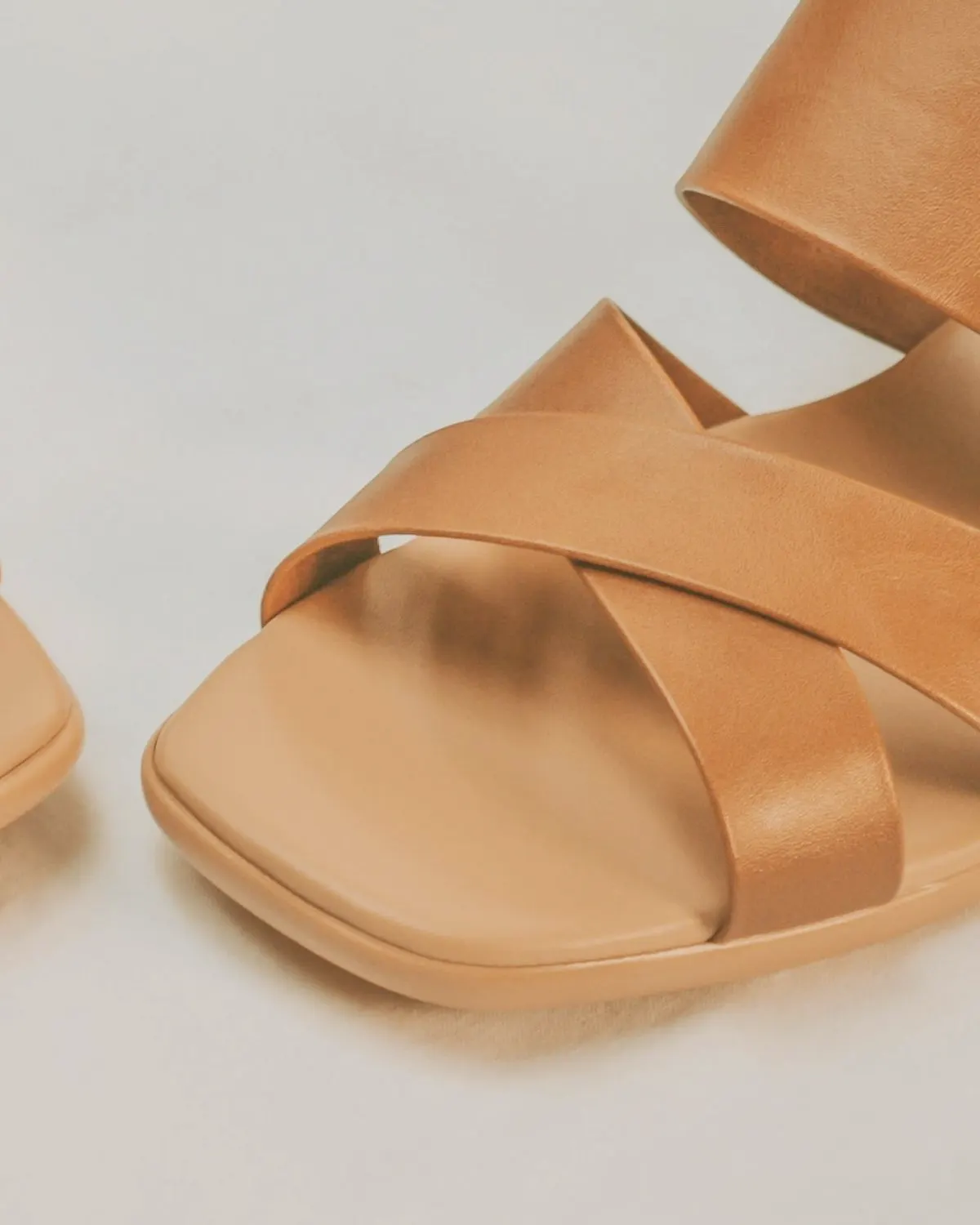 Tan leather cross-strap sandal on a pale background