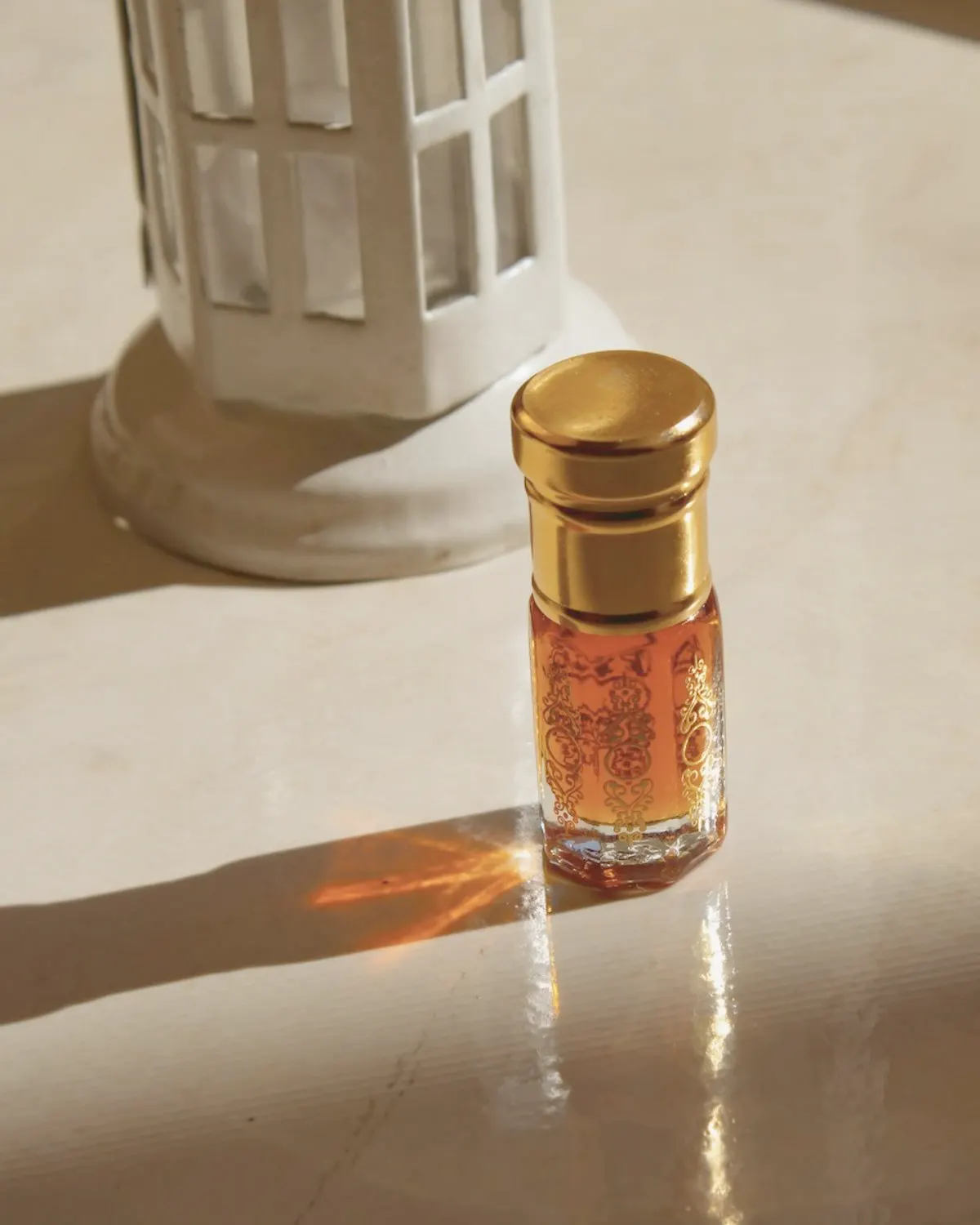 Small gold-capped bottle of oud oil beside an incense burner